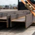 Close-up of steel beams strapped with bright orange tie-downs on a flatbed trailer representing secure flatbed trucking load handling